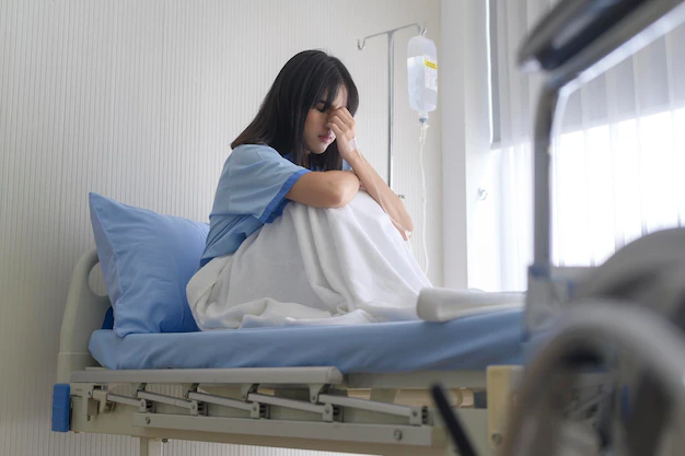 A female patient is sitting on bed in hospital