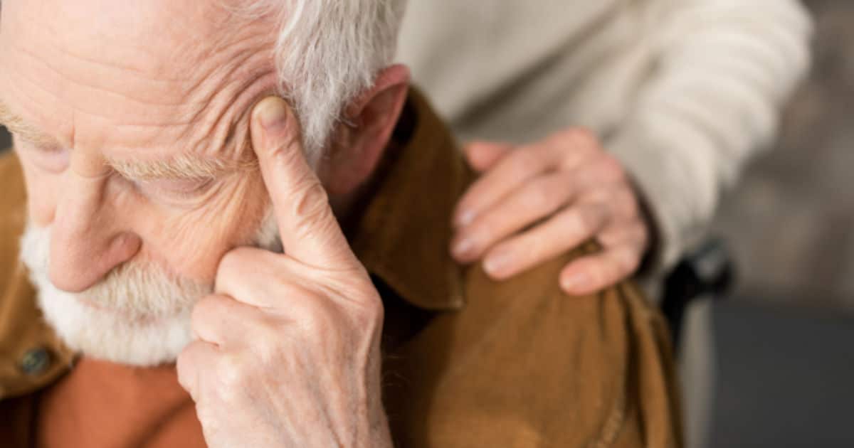 An elderly man placing a finger on the side of his head