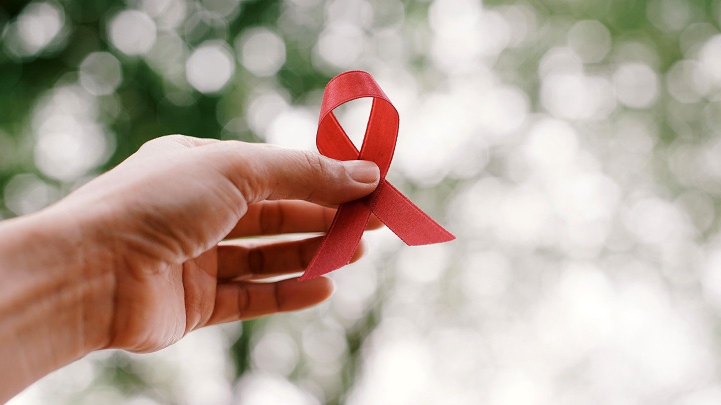 A Caucasian hand holding the red ribbon which is the solidarity of people living with HIV/AIDS