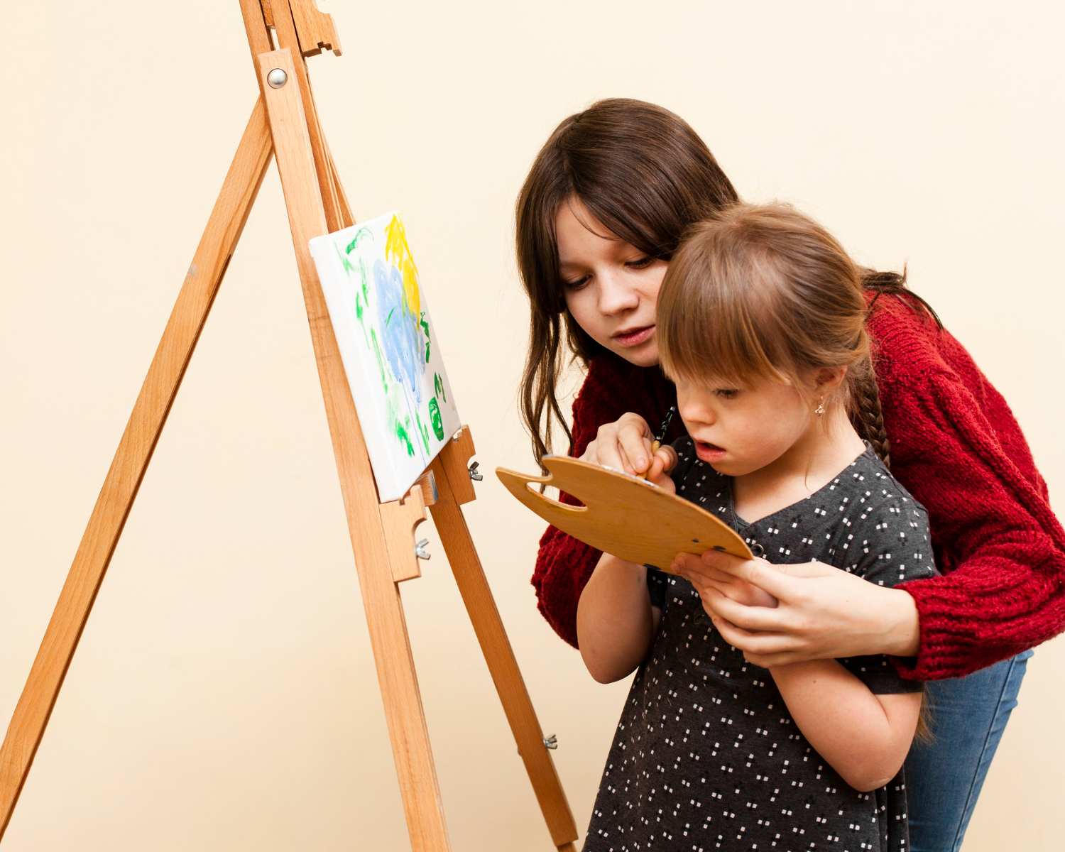 A girl is helping a little girl with down syndrome in painting.