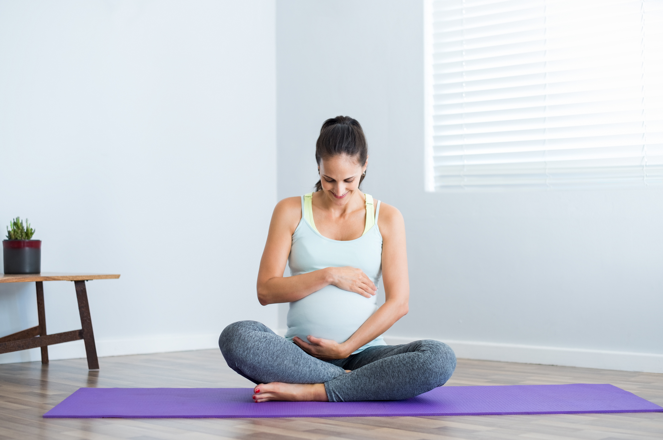 A preganant woman sitting on a purple yoga mat holding her belly with both hands