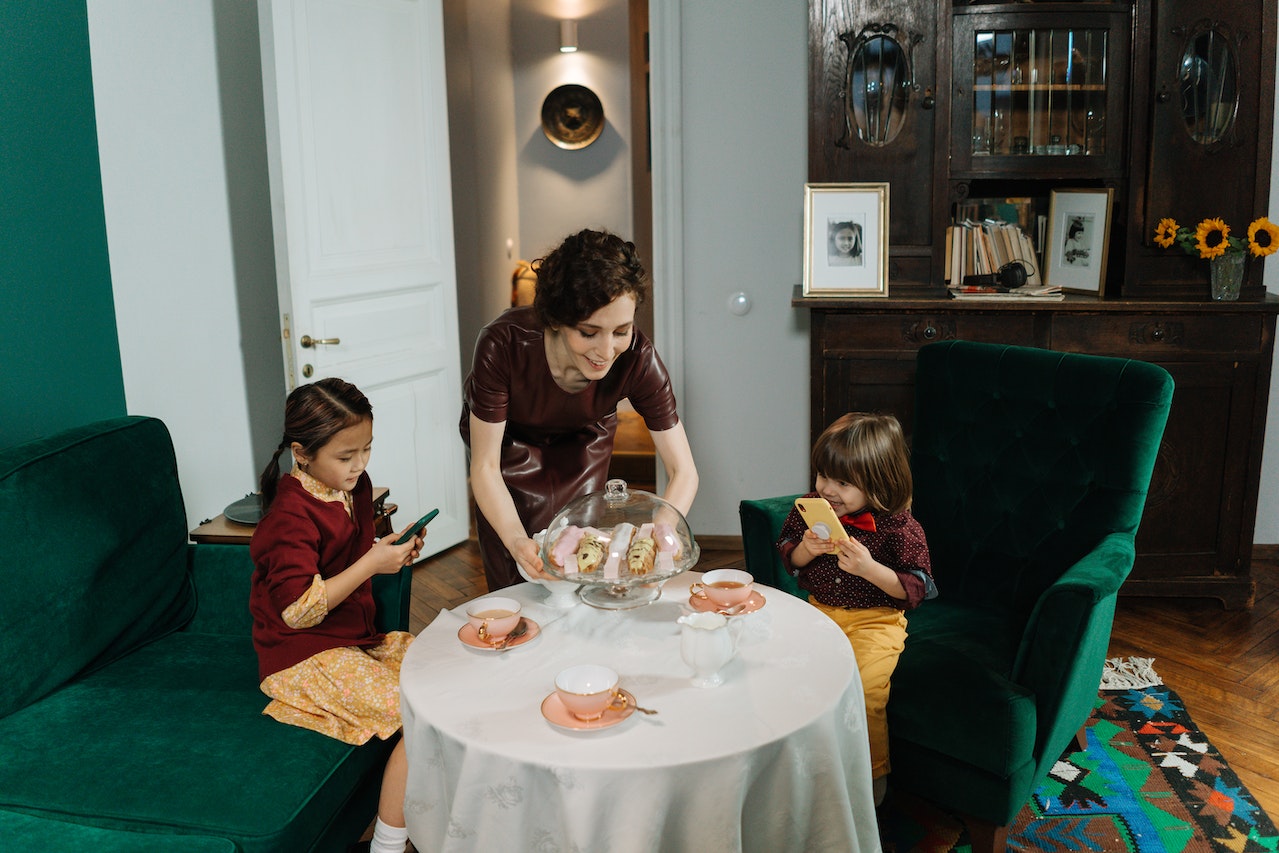 A Woman Serving The Kids Sitting at the Table With Sandwiches