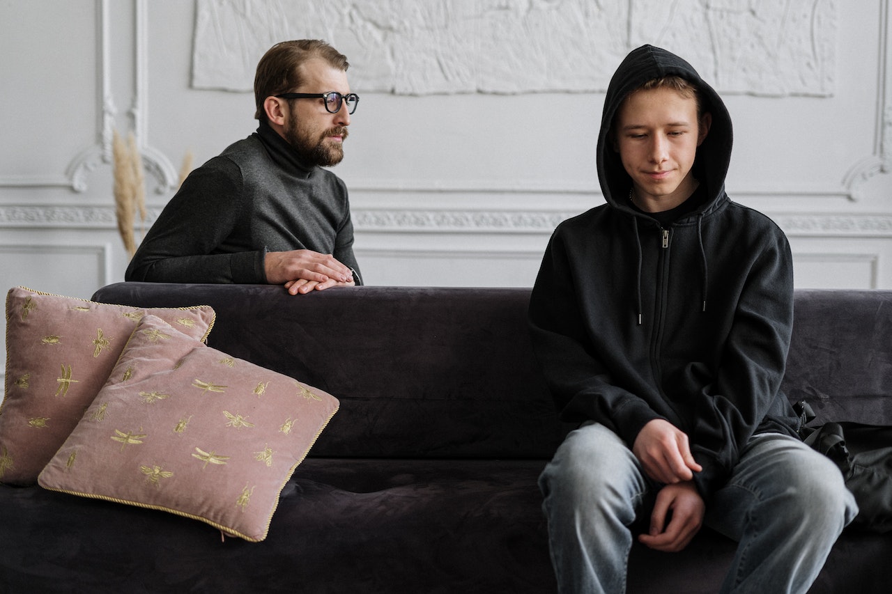 Young Man in Black Hoodie Sitting With His Father on a Couch