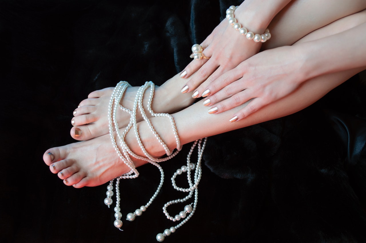 Crop anonymous woman legs and hands in pearl jewelry