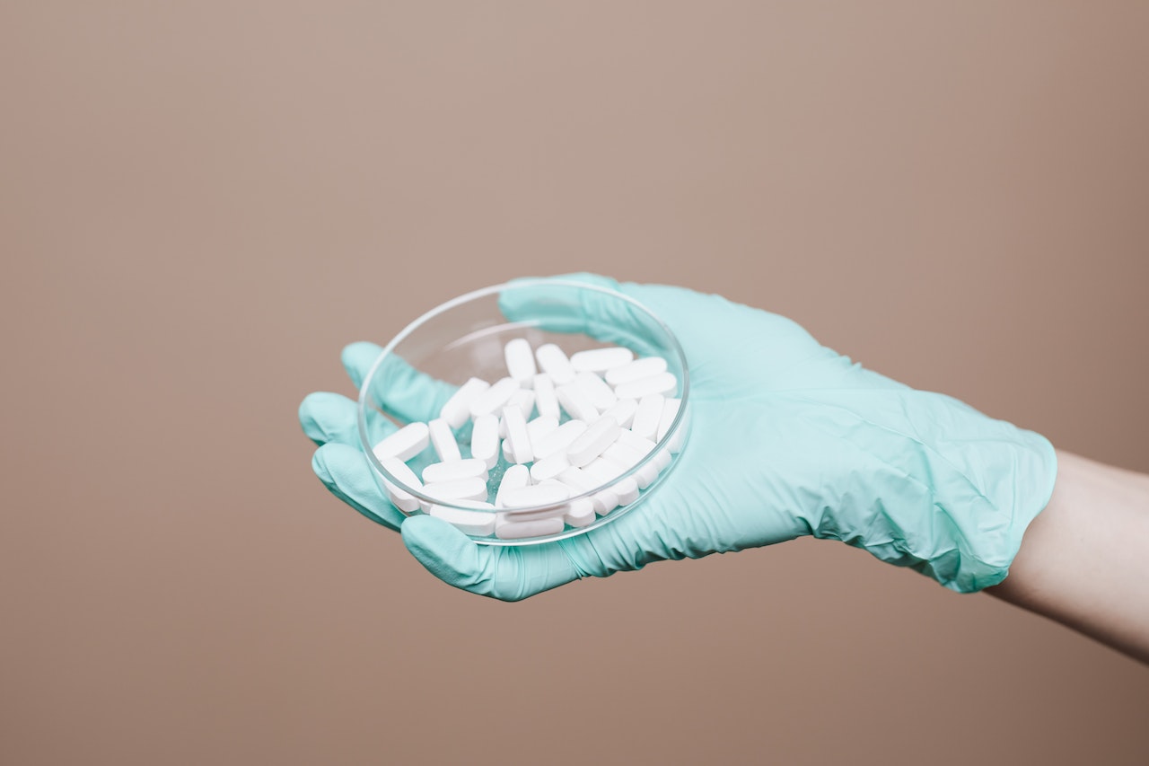 A Gloved Hand Holding White Tablets on Petri Dish