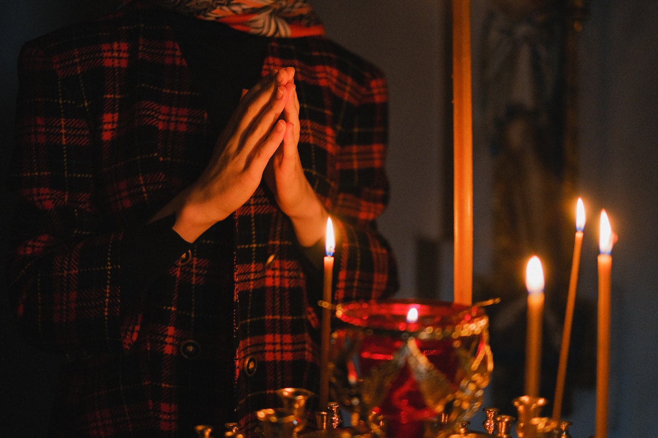 Person in Red and Black Plaid Long Sleeve Shirt Praying Before Lighted Candles
