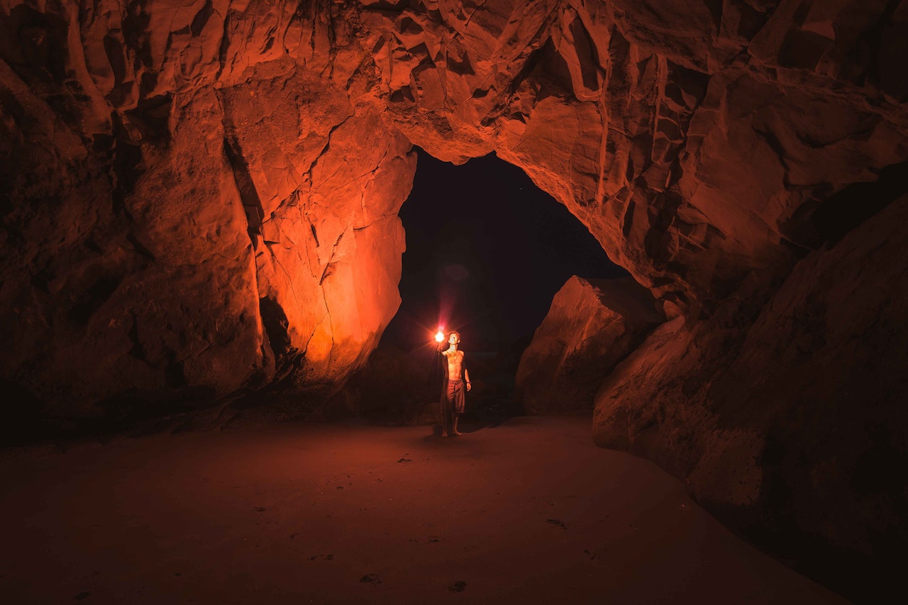 Person Standing and Holding A Lamp Inside A Cave