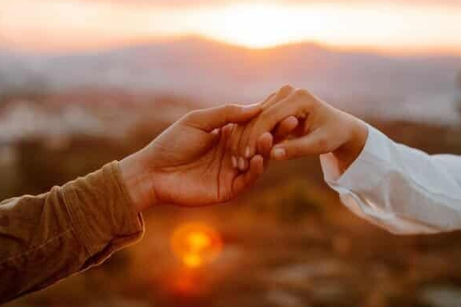 A man and a woman hold hands in front of the sunset