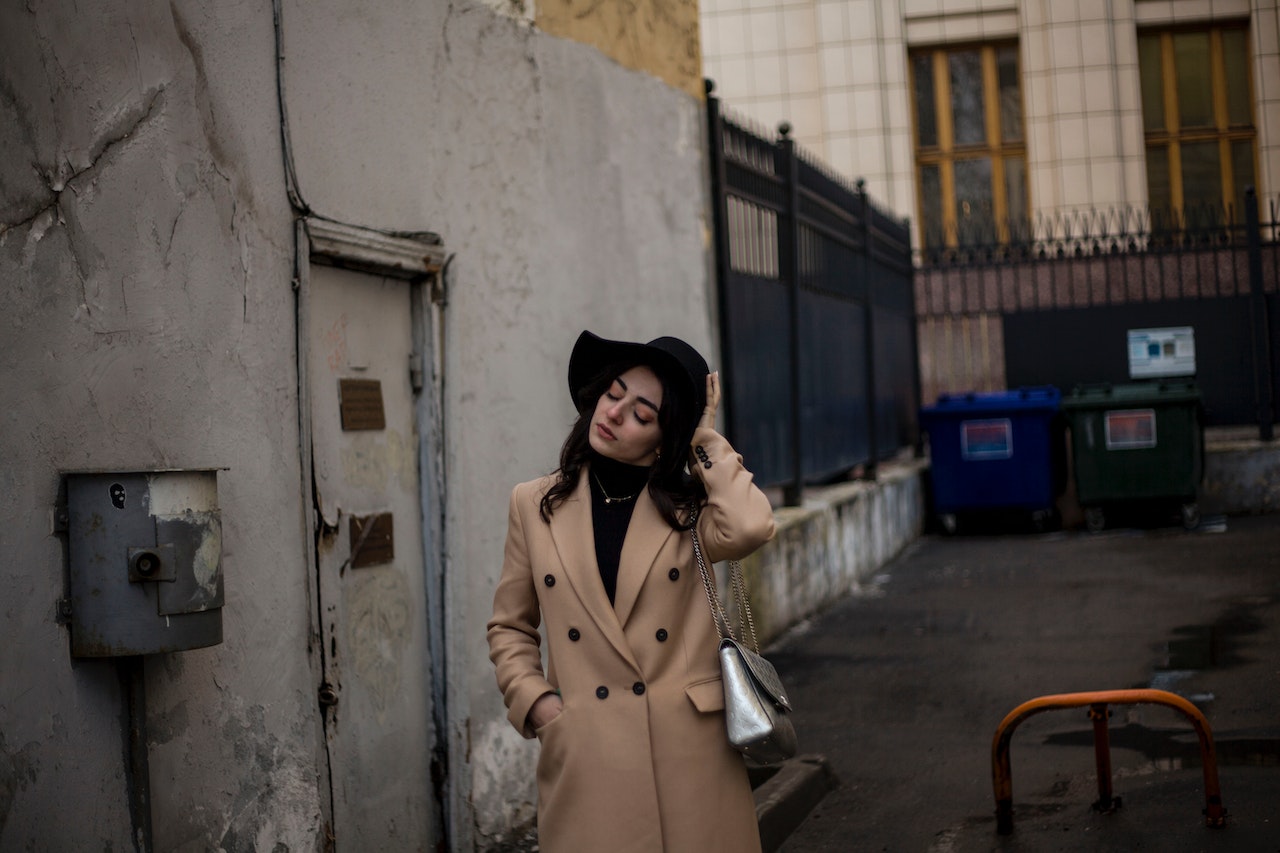 Woman in Beige Coat Wearing Black Hat Standing Beside A Back Door