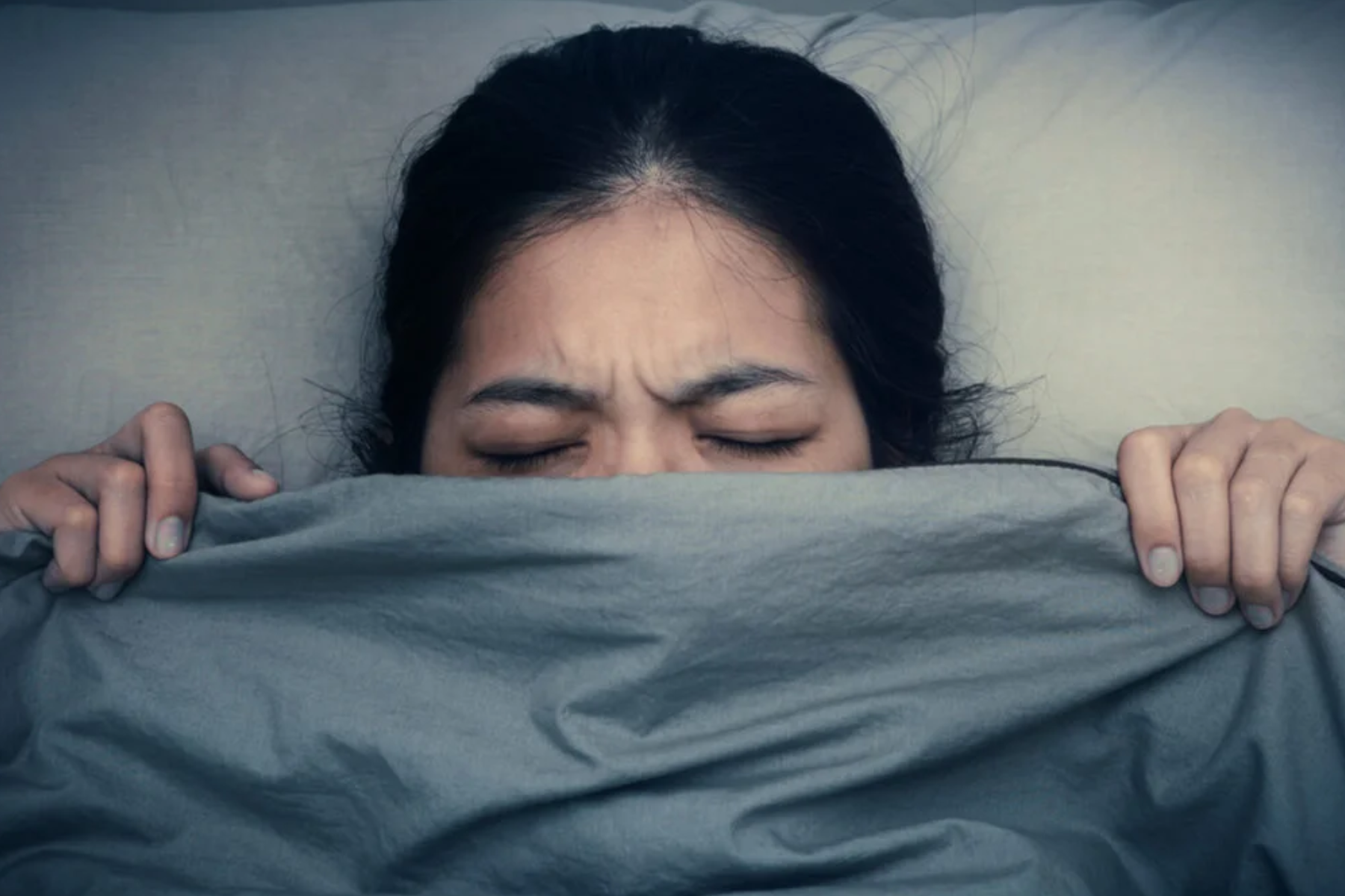 A woman covers half of her face with a bed sheet