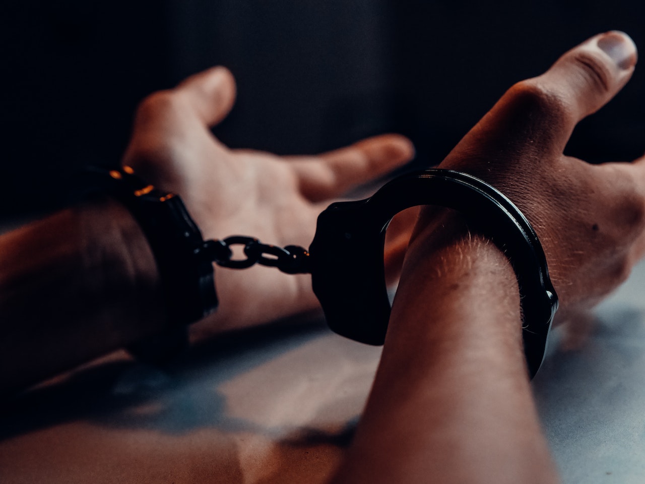 A Person's Hands on the Table Wearing Handcuffs