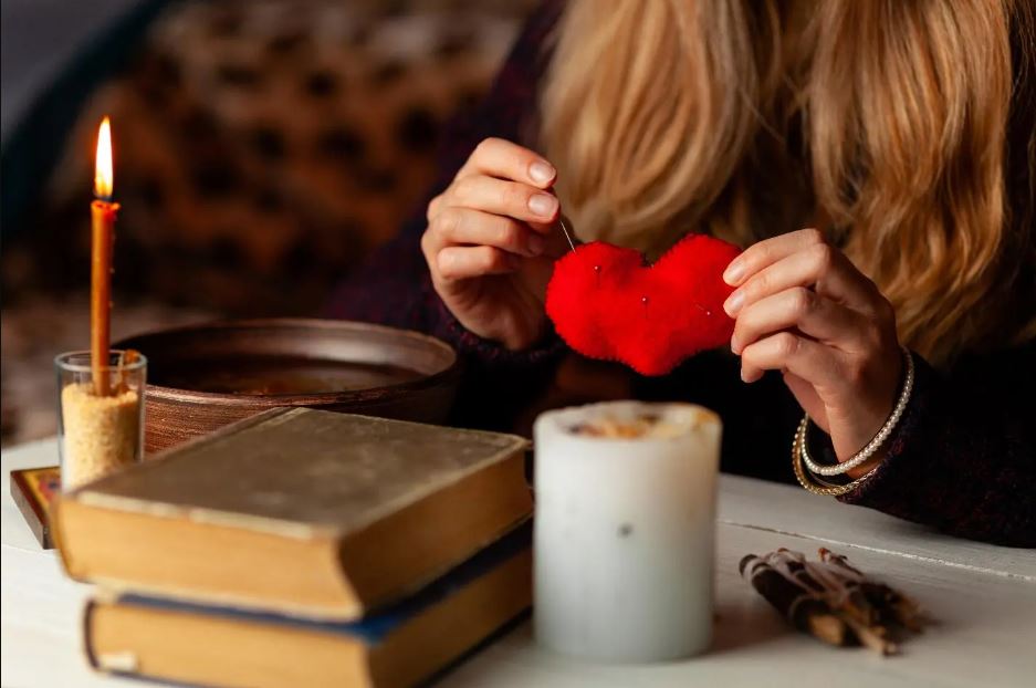 A lady holding a red object in the form of love above a white candle with two books on the table before her