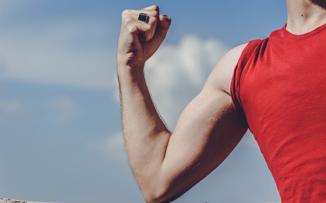 Man Wearing A Red Shirt Is Flexing His Muscles On His Right Arm
