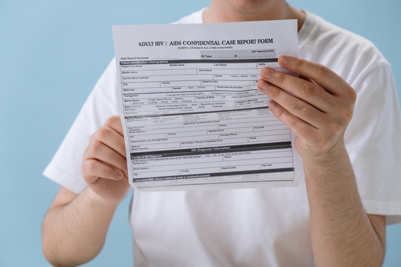 A man wearing a white tshirt holding an AIDS Confidential Case Report Form