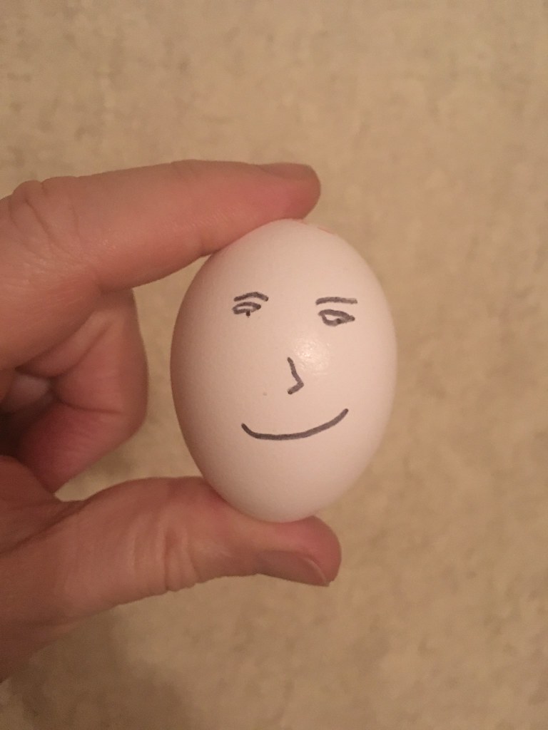 An egg is held in hand and emoji is drawn on it