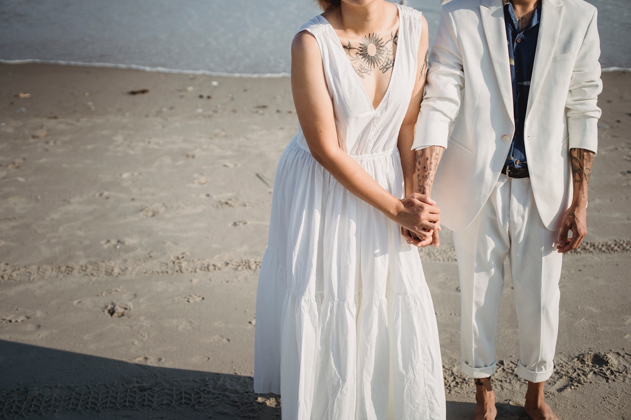 Woman in White Sleeveless Dress Standing on the Beach With A man In White Suit