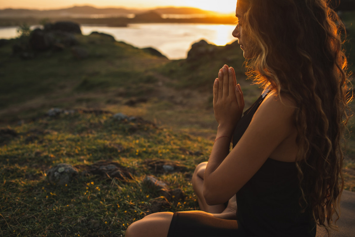 A woman sitting in the meditation pose praying alone at sunrise in nature