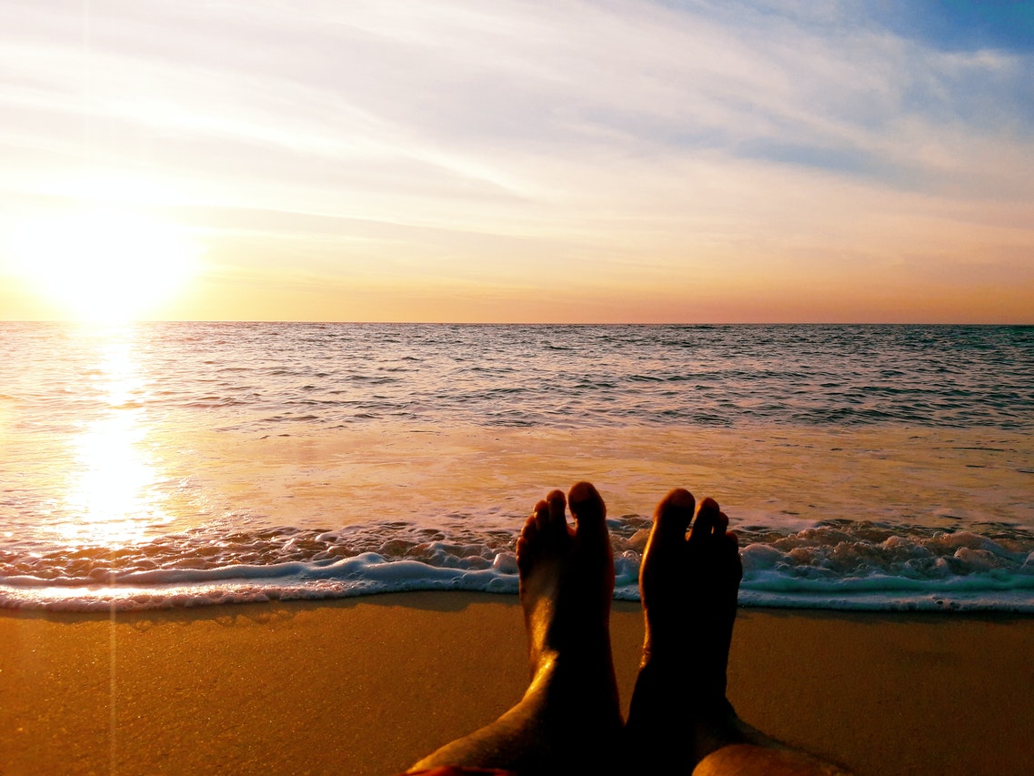 Person Shows His Feet Relaxing In The Beach During Sunset