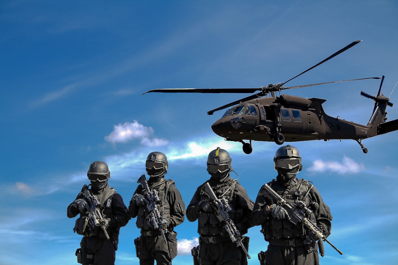Four Soldiers Carrying Rifles And A Flying Helicopter Under The Blue Sky