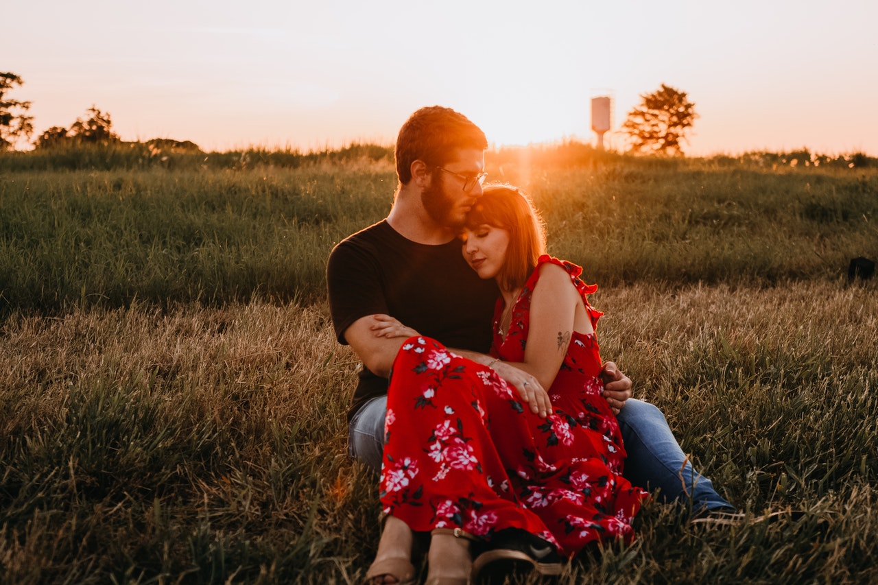 Man in Black Crew Neck T-shirt Sitting on Grass Field Beside Woman in Red Floral Dress