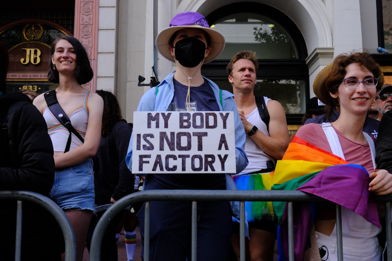 A man holding a 'My body is NOT a factory' sign at a pride march
