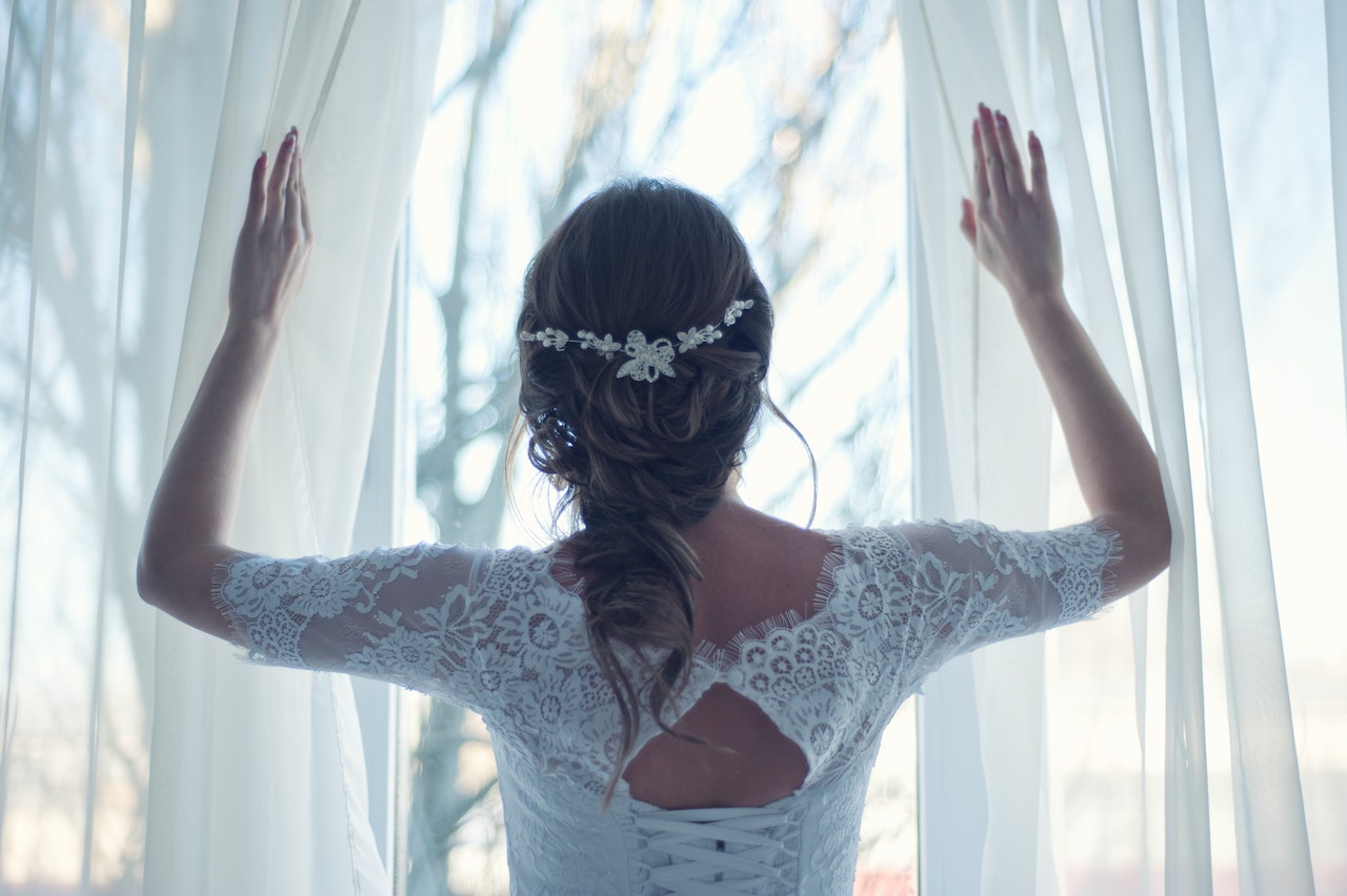 Bride Spreading white curtains while looking outside a window