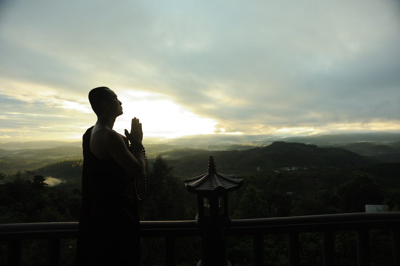 Monk Holding A Rosary While Praying In A Veranda Overlooking The Mountains
