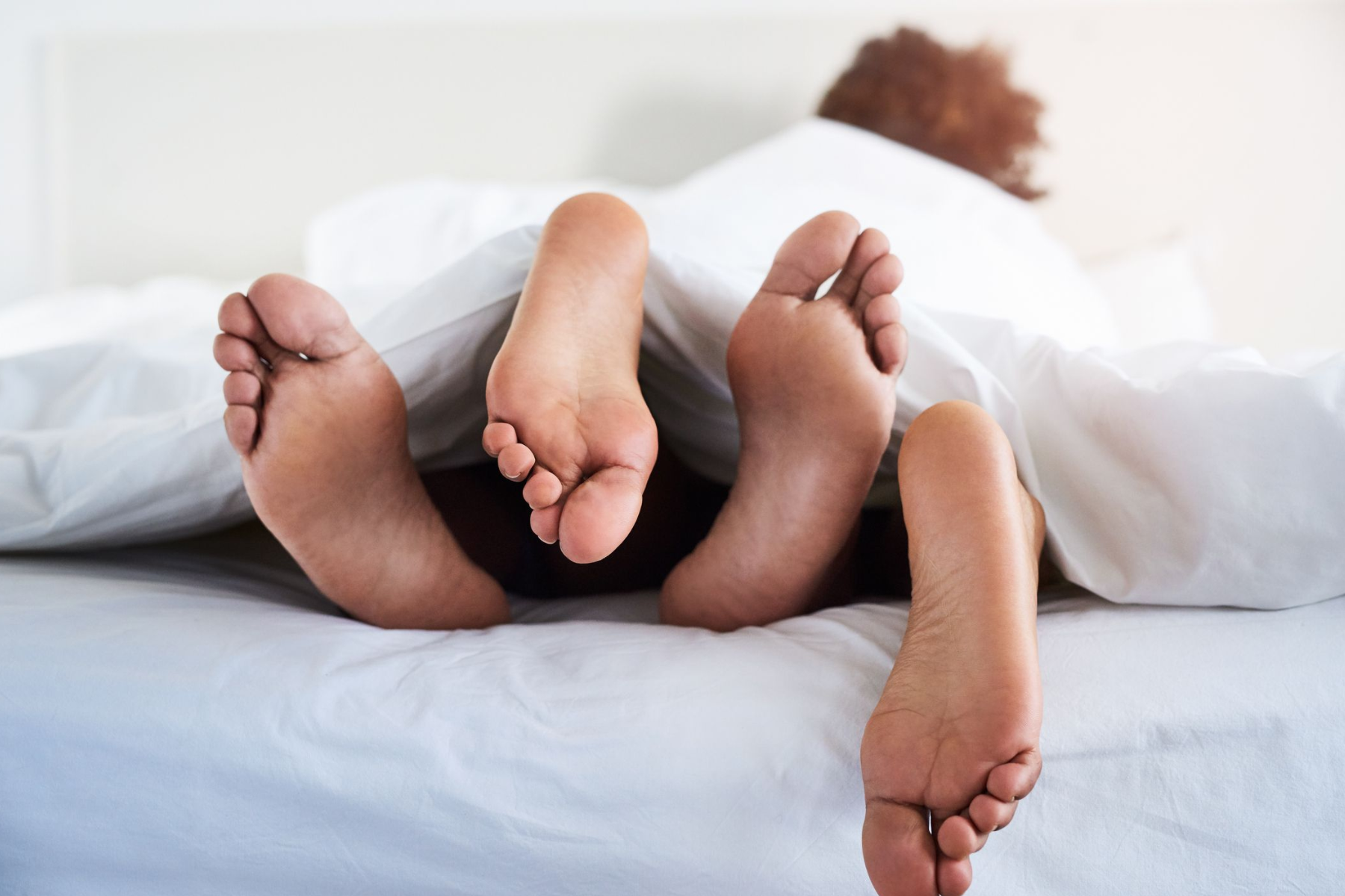 A man and a woman's feet are hidden beneath the bed sheet