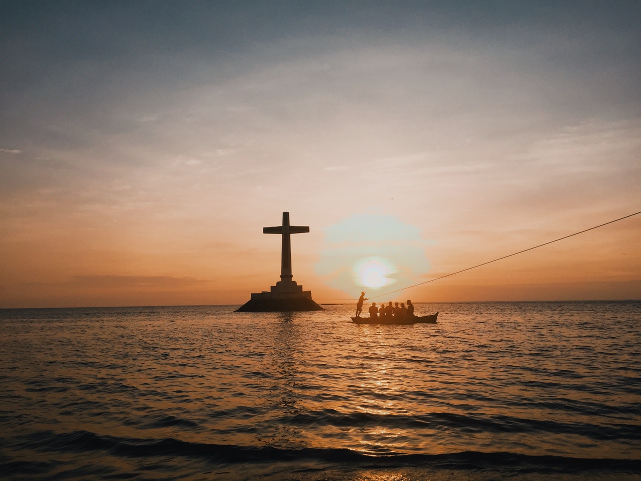 Cross And Boat Full Of People In An Ocean During Dawn