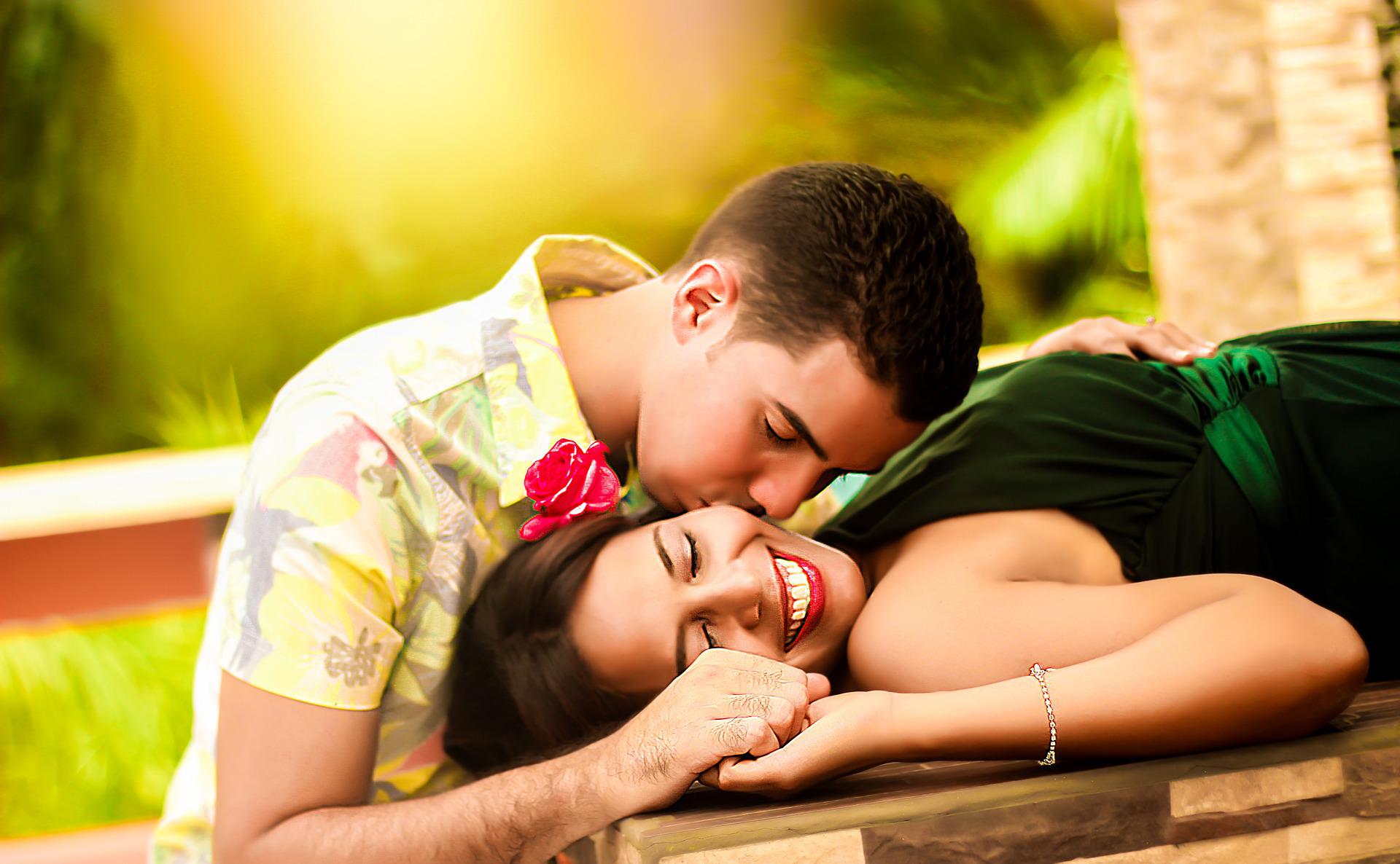 A woman lying on a wooden table while being kissed by his boyfriend