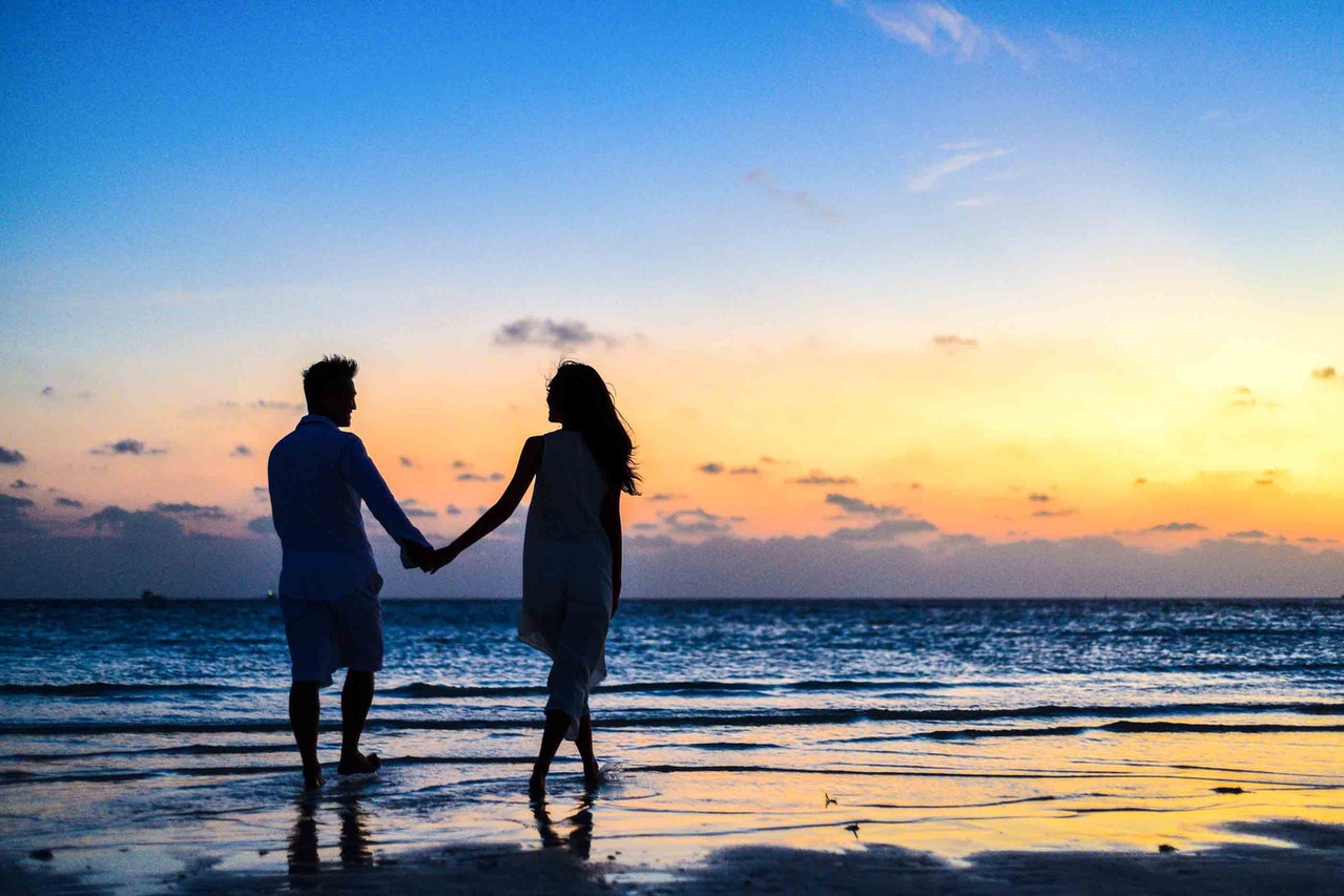Man And Woman Holding Hands While Walking On Seashore During Sunrise