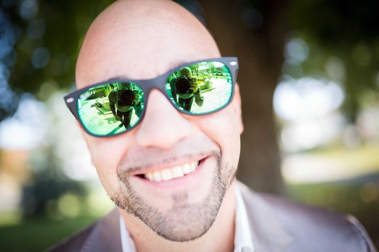 A Bald Man in Gray Top Wearing Green Sunglasses With Black Frames
