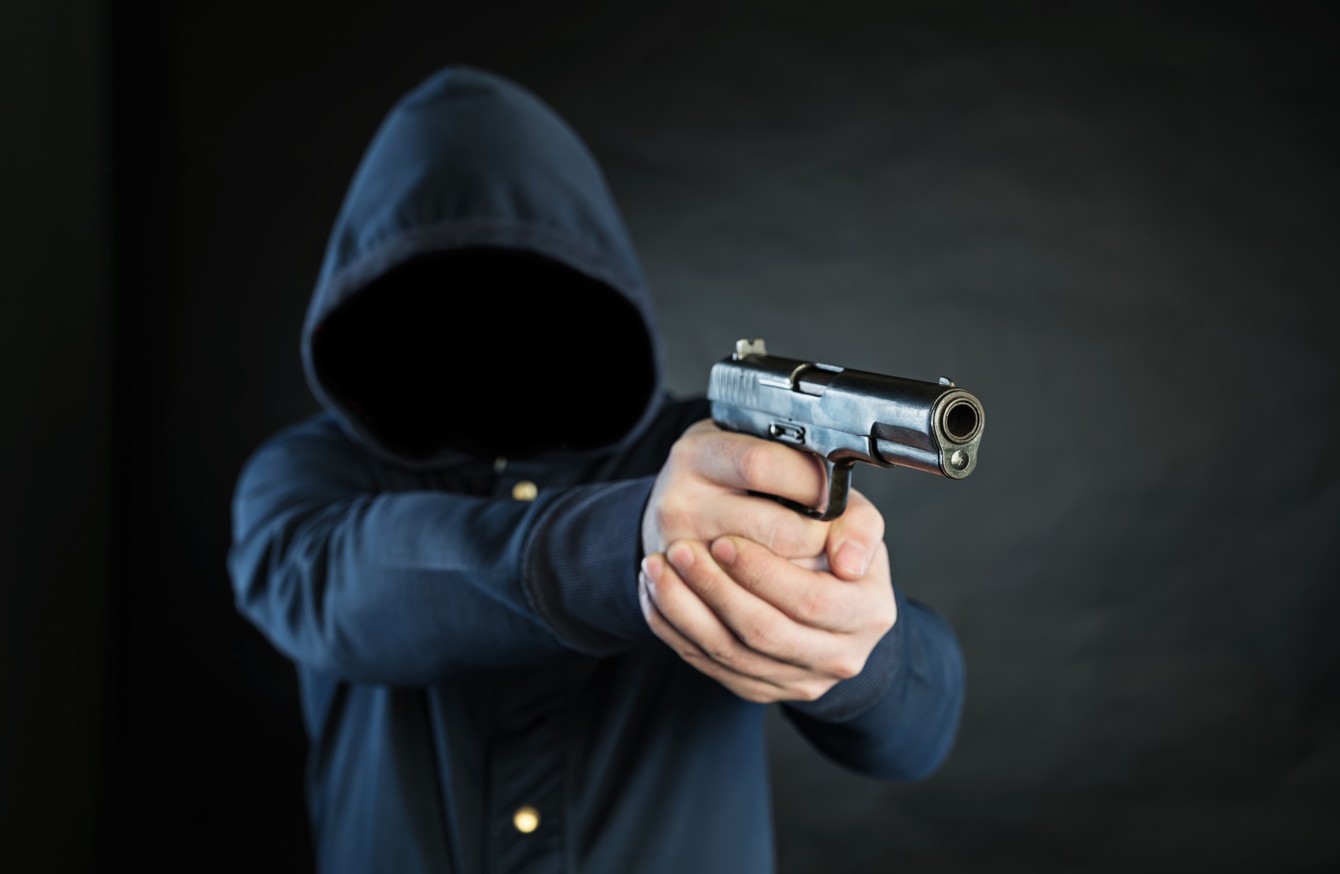 A gun being held by a man wearing a hoodie without a face