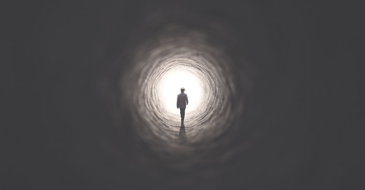 A man walking towards a hole that has white light