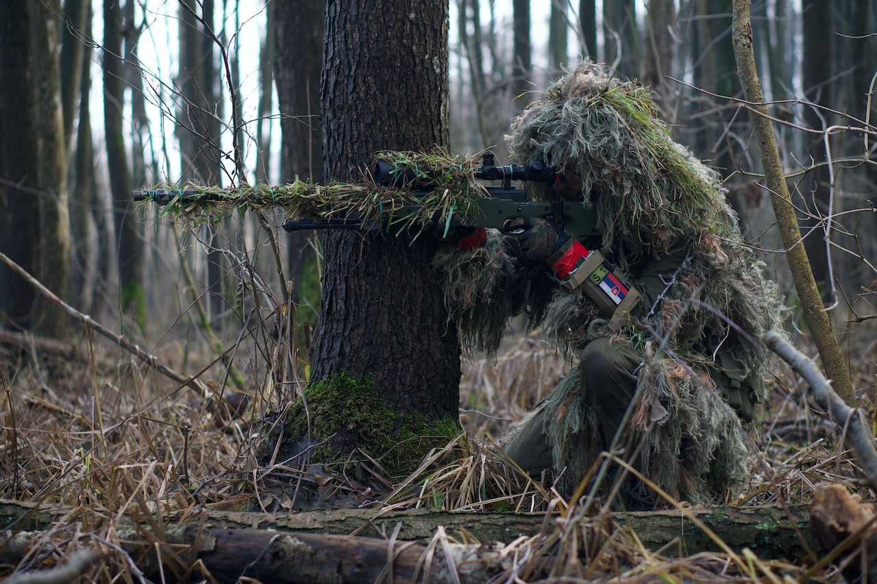 A Soldier Sniper Aiming Though The Rifle Scope In The Forest