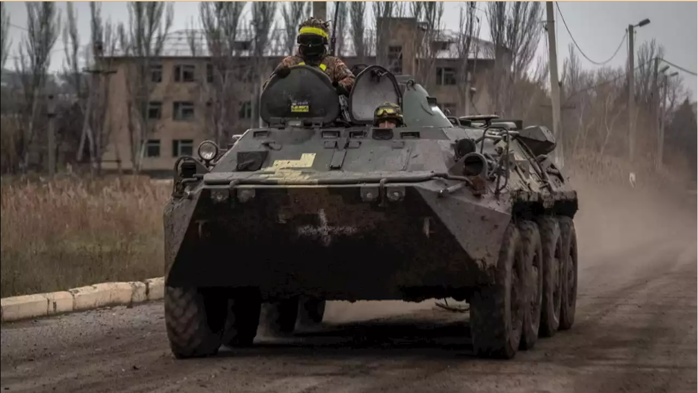 A war tank moving on the road with a soldier on top