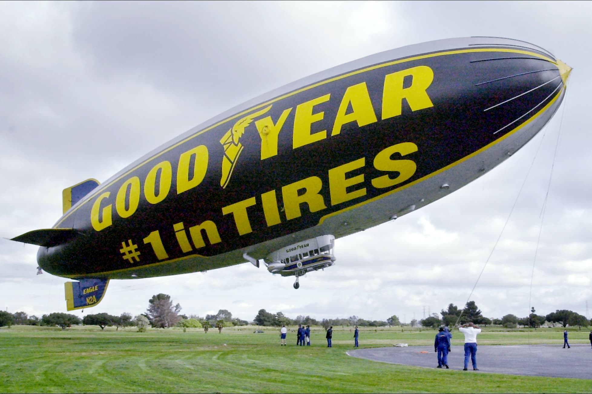 A big blimp may in the sky with people underneath it