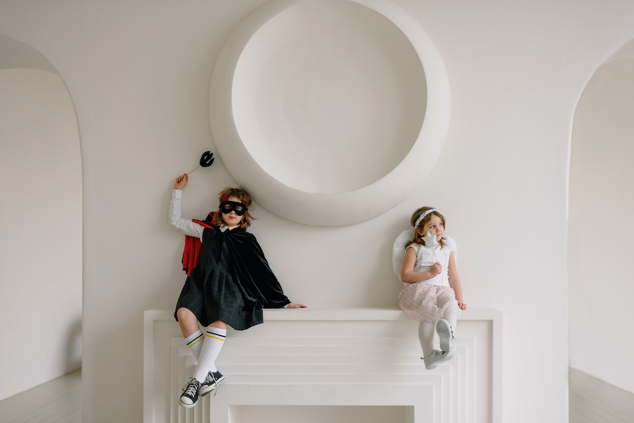 Two Children in Costumes Leaning on a White Wall