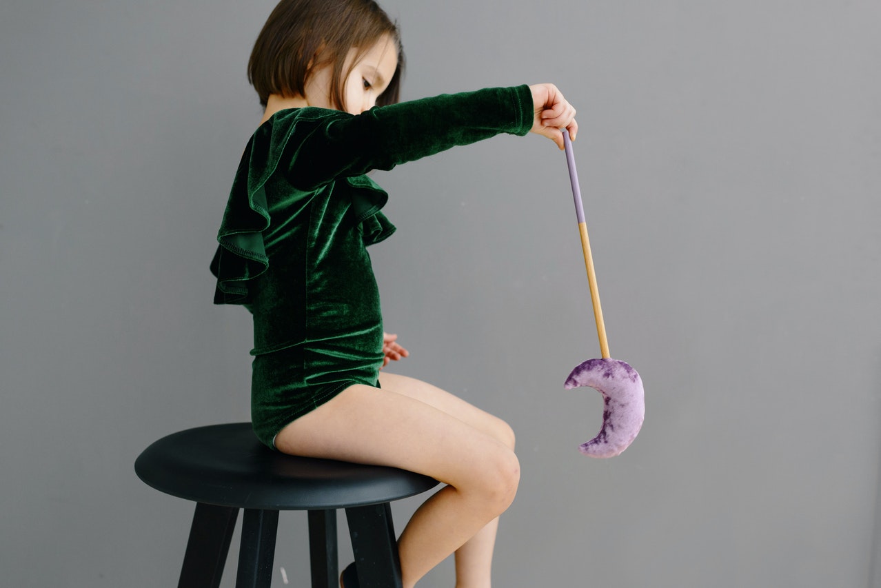A Young Girl in Green Bodysuit Sitting on the Chair while Holding a Moon Wand