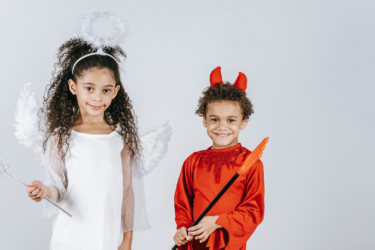 Cute little black children in angel and devil costumes smiling at camera in white studio