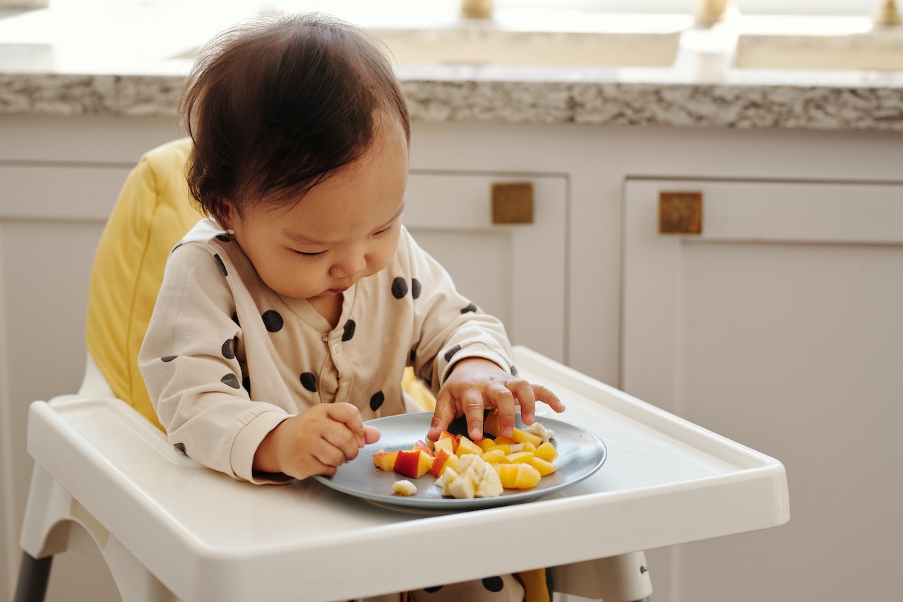 A Child Sitting on a Baby High Chair While Eating Fruits