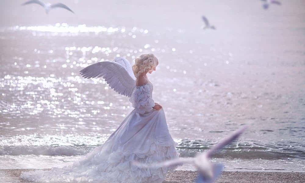 Girl In White Dress And Wings Walking On Sea Shore
