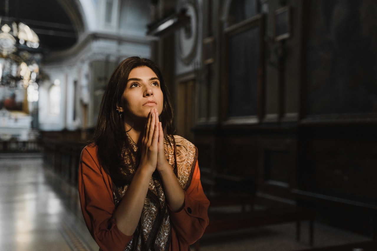 Woman Praying In The Church In Orange Coat With Black And Brown Scarf
