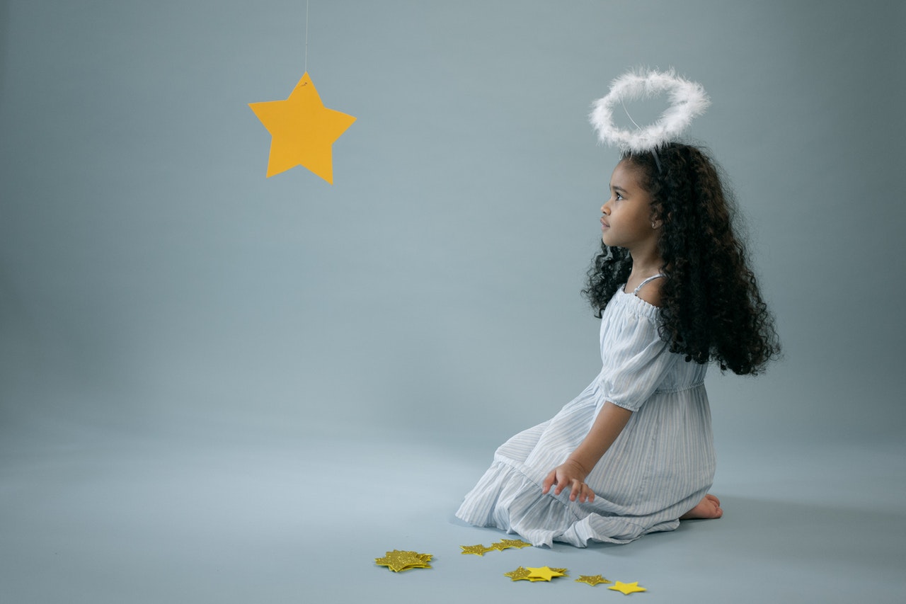 Adorable black girl in angel costume near hanging star