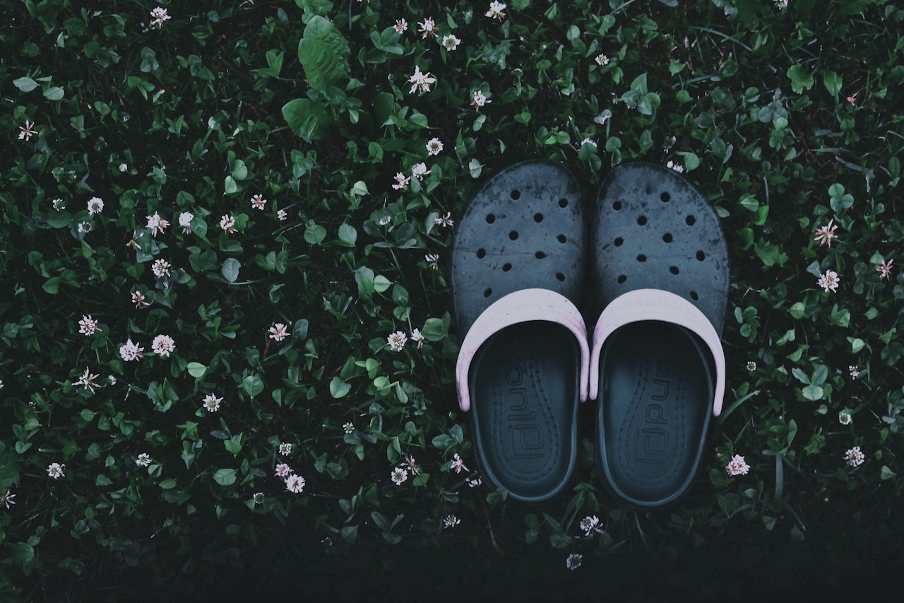 A Pair Of Rubber Croc Clogs on Top of Leaves And Flowers