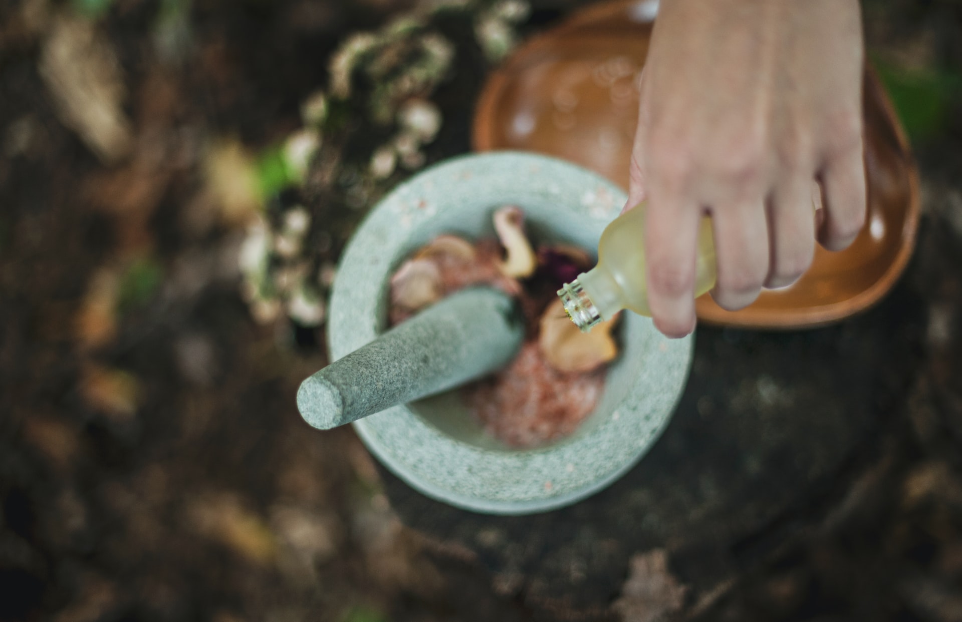 A person's hand pouring oil into a mixture into a mortar and pestle