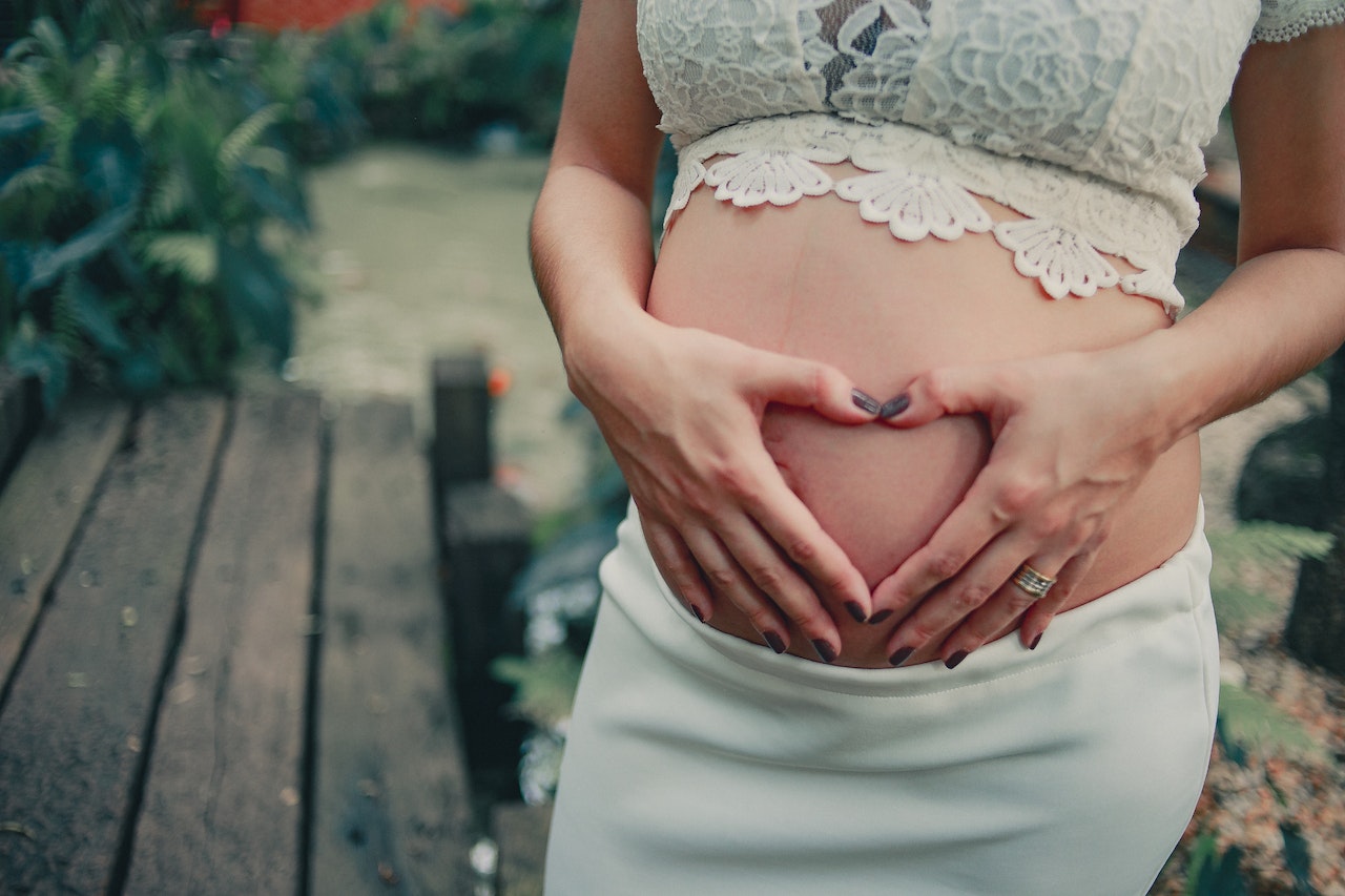 Pregnant Woman Wearing White Skirt And Lacy Bra While Holding Her  Baby Bump