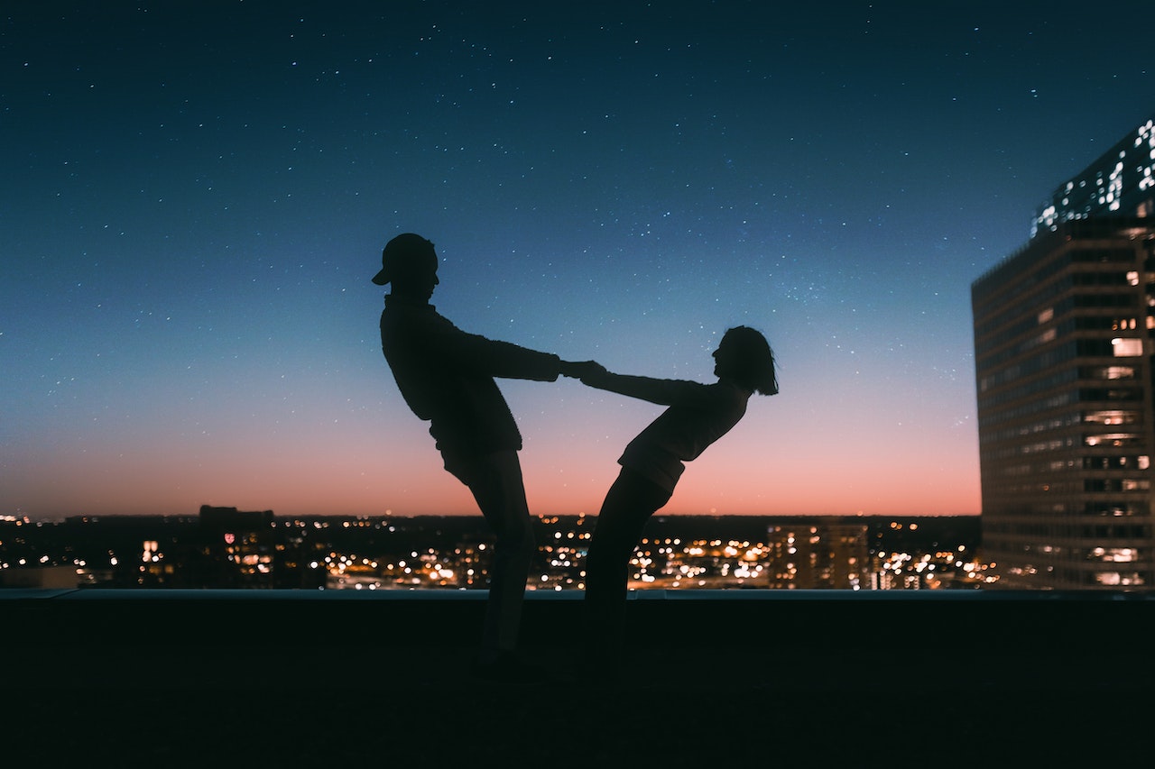 Silhouette of a man and a woman holding on the each other's hands in the rooftop overlooking the city