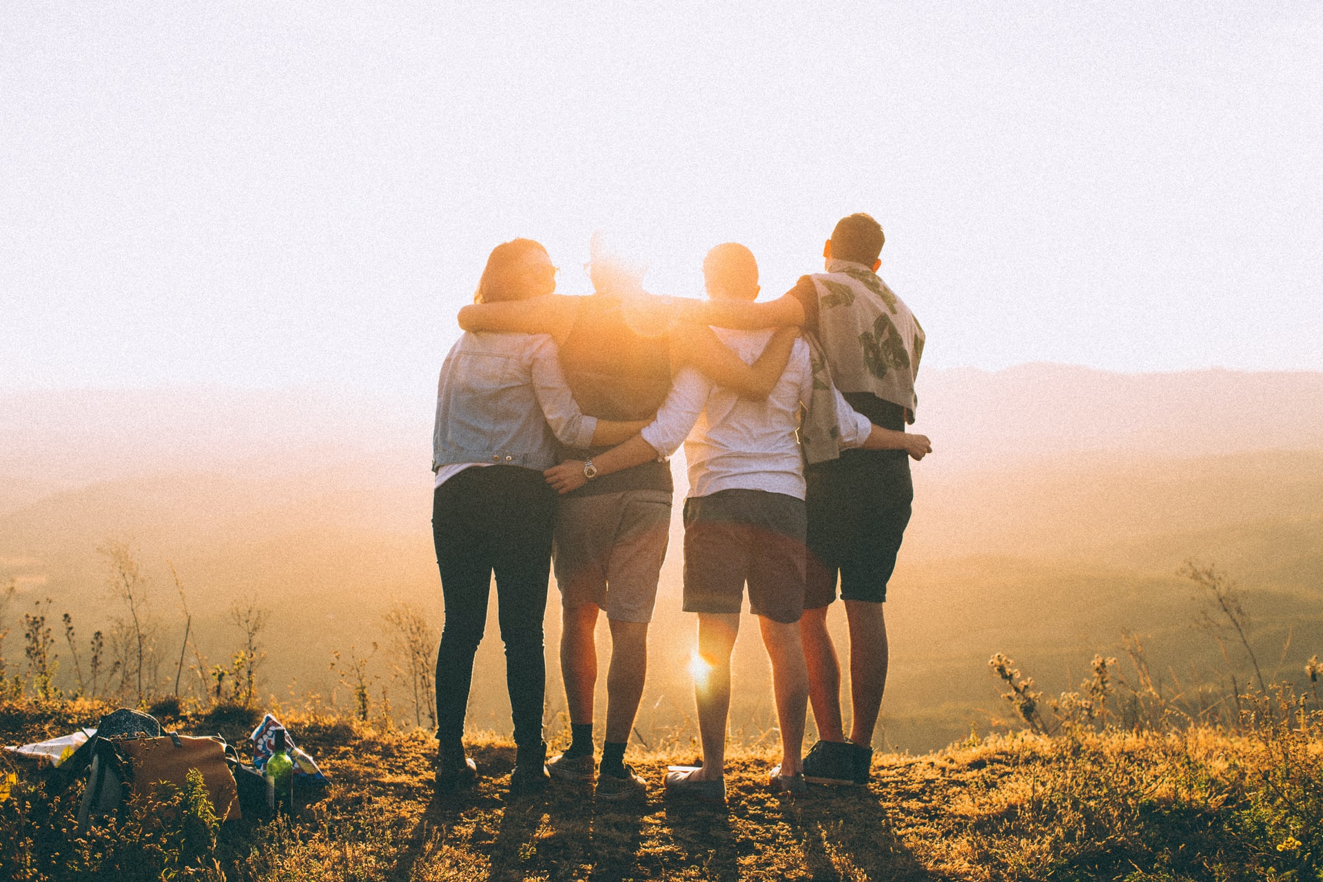 Four persons with hands wrapped around their shoulders are looking at the sunset