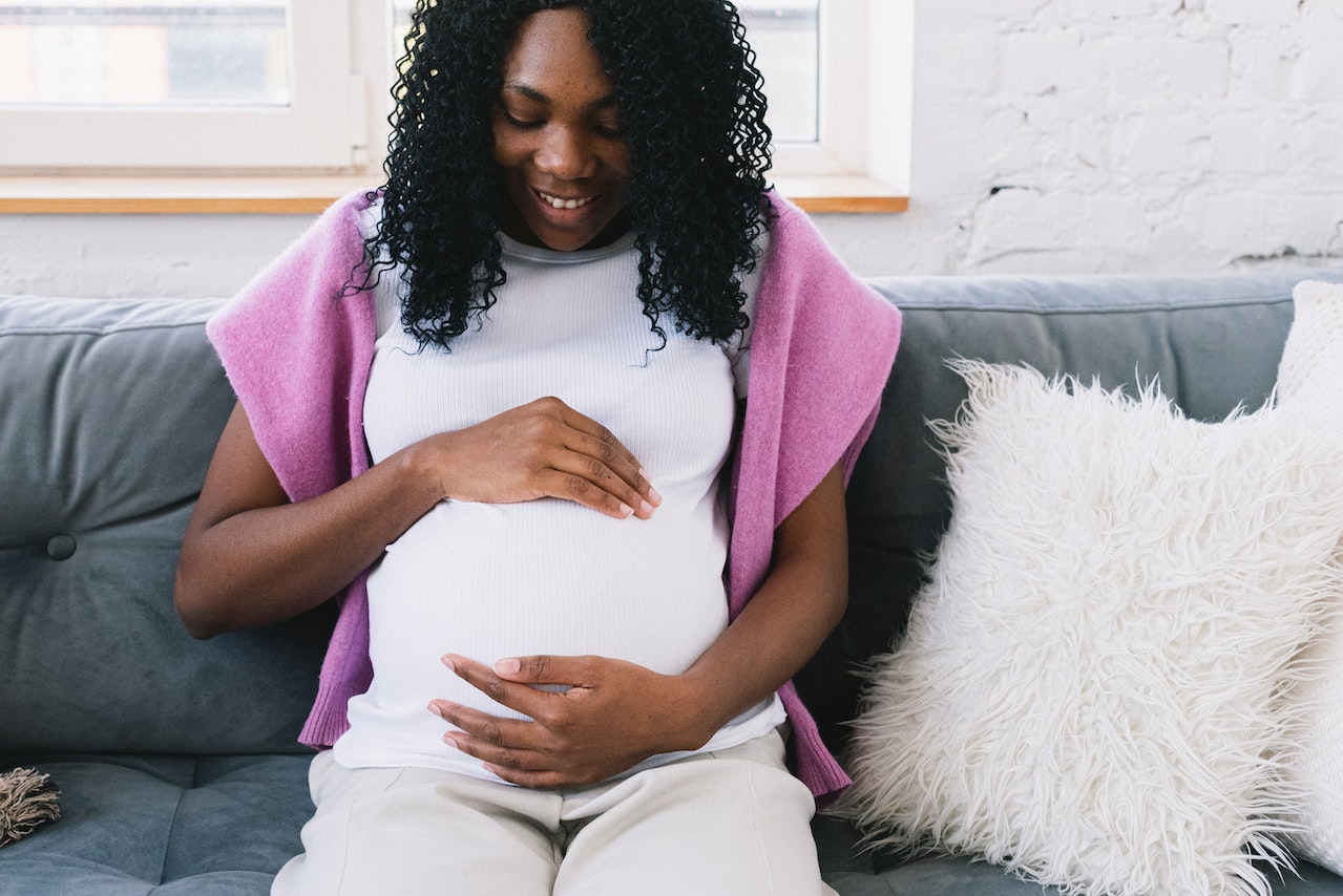 Happy pregnant black woman sitting on couch